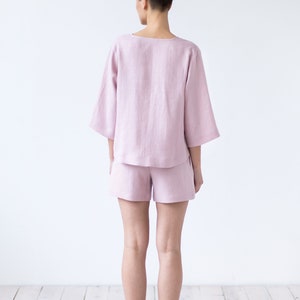 May include: A woman wearing a light pink linen pajama set with a short-sleeved top and shorts. The set is made of a soft, breathable fabric and is perfect for lounging around the house.