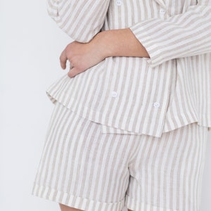 May include: A double-breasted blazer and matching shorts set featuring a vertical striped pattern in beige and white. The blazer has a notched lapel and four small white buttons, while the shorts have a cuffed hem design.