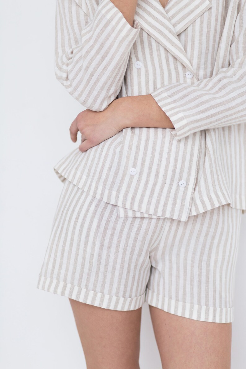 May include: A double-breasted blazer and matching shorts set featuring a vertical striped pattern in beige and white. The blazer has a notched lapel and four small white buttons, while the shorts have a cuffed hem design.