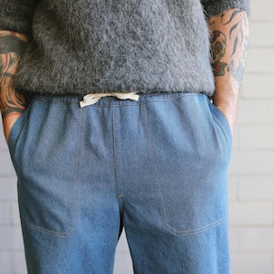 Puede incluir: Pantalones vaqueros azul claro con cintura con cord&oacute;n y bolsillos delanteros. Los pantalones se combinan con un su&eacute;ter gris de manga corta y texturizado. El modelo tiene tatuajes en los brazos. Ropa casual.