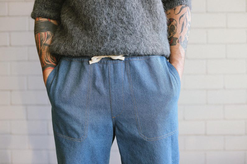 Puede incluir: Pantalones vaqueros azul claro con cintura con cord&oacute;n y bolsillos delanteros. Los pantalones se combinan con un su&eacute;ter gris de manga corta y texturizado. El modelo tiene tatuajes en los brazos. Ropa casual.