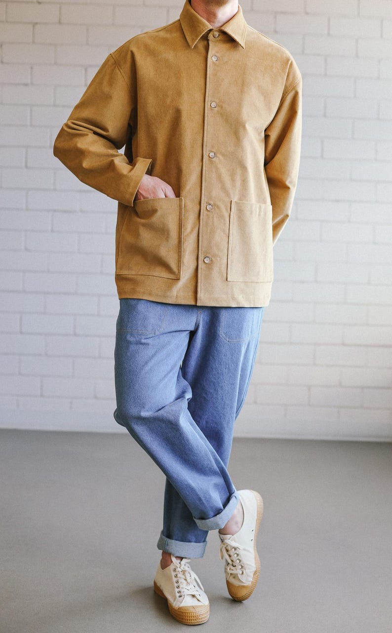 Puede incluir: Una persona vestida con una chaqueta abotonada color beige con dos bolsillos delanteros y vaqueros azul claro. La persona tambi&eacute;n lleva zapatillas blancas con suelas beige. El atuendo es informal y elegante.