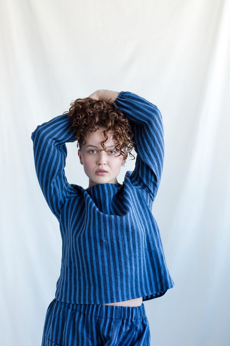 May include: A long-sleeved top and matching bottoms featuring a vertical striped pattern in alternating shades of dark blue and medium blue. The top has a round neckline and loose-fitting sleeves, while the bottoms feature an elasticized waistband.