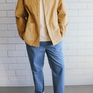 Puede incluir: Chaqueta de pana color canela con dos bolsillos delanteros y botones, combinada con una camiseta crema y vaqueros azul claro. El conjunto se completa con zapatillas blancas con suela color canela. El modelo est&aacute; de pie frente a una pared de ladrillos blancos.
