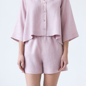 May include: A light pink linen pajama set with a button-up top and shorts. The top has a v-neck and the shorts have a relaxed fit.