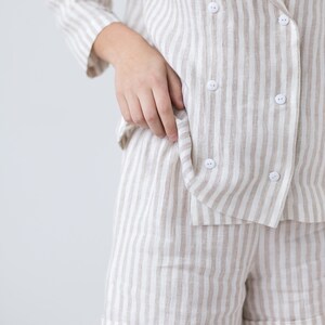 May include: A double-breasted blazer and matching shorts set featuring a vertical beige and white striped pattern. The blazer has a wide lapel, three-quarter length sleeves, and six small white buttons arranged in two columns on the front.