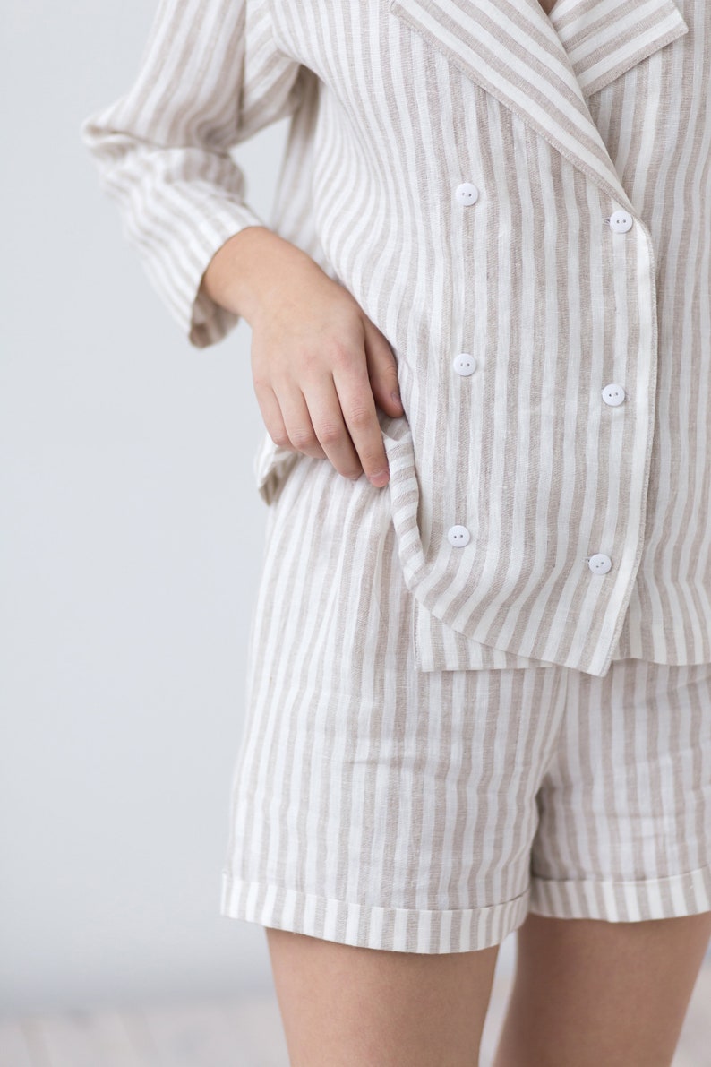 May include: A double-breasted blazer and matching shorts set featuring a vertical beige and white striped pattern. The blazer has a wide lapel, three-quarter length sleeves, and six small white buttons arranged in two columns on the front.