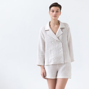 May include: A two-piece lounge set consisting of a long-sleeved, double-breasted button-down shirt with a notched collar and matching shorts, both featuring a vertical beige and white striped pattern made from a textured fabric.