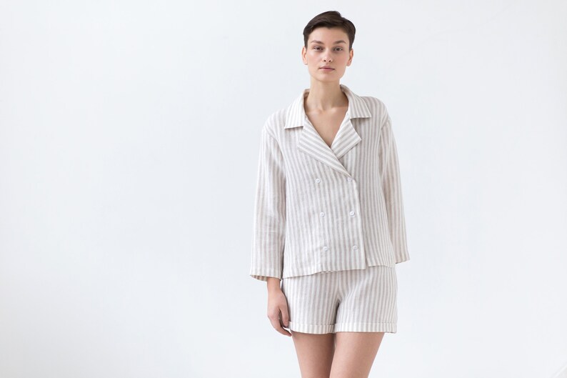 May include: A two-piece lounge set consisting of a long-sleeved, double-breasted button-down shirt with a notched collar and matching shorts, both featuring a vertical beige and white striped pattern made from a textured fabric.