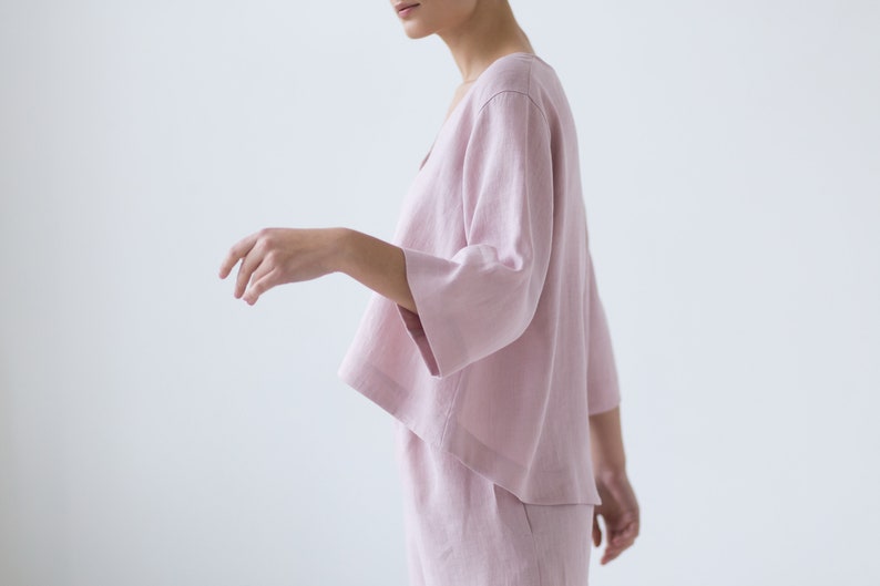 May include: A pale pink linen top with a relaxed fit and three-quarter sleeves. The top has a V-neckline and a slightly cropped hem.