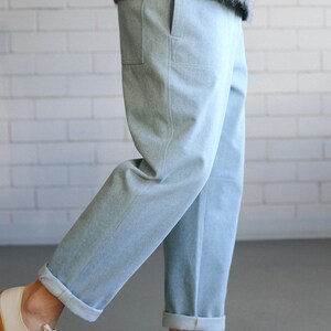 May include: Light blue denim pants with cuffed hems and a relaxed fit. The pants are paired with off-white canvas sneakers with brown soles. The person is wearing a gray sweater.