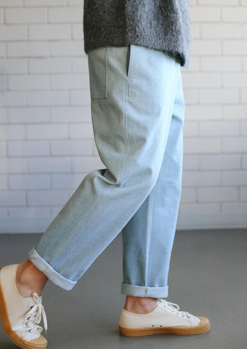 May include: Light blue denim pants with cuffed hems and a relaxed fit. The pants are paired with off-white canvas sneakers with brown soles. The person is wearing a gray sweater.