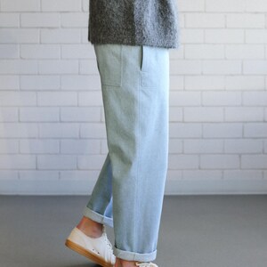 May include: Light blue trousers with a straight-leg fit, featuring side pockets and cuffed hems, paired with a fuzzy gray sweater and white canvas sneakers with gum-colored rubber soles and textured toe caps.