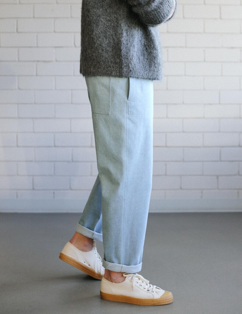 May include: Light blue trousers with a straight-leg fit, featuring side pockets and cuffed hems, paired with a fuzzy gray sweater and white canvas sneakers with gum-colored rubber soles and textured toe caps.