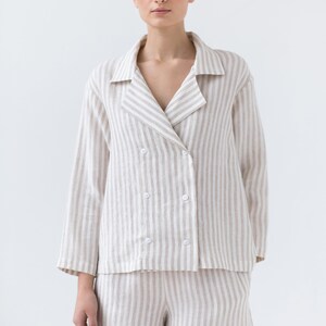 May include: A double-breasted long-sleeve jacket with a notched collar and four white buttons, paired with matching shorts. Both pieces feature a vertical striped pattern in light beige and white, creating a coordinated two-piece set.