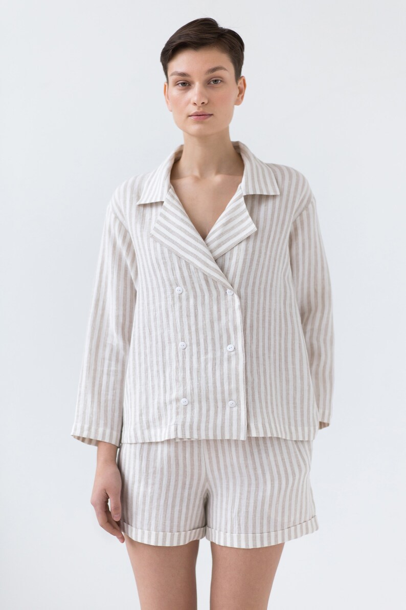 May include: A double-breasted long-sleeve jacket with a notched collar and four white buttons, paired with matching shorts. Both pieces feature a vertical striped pattern in light beige and white, creating a coordinated two-piece set.