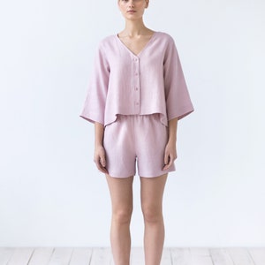 May include: A woman wearing a light pink linen pajama set with a button-up top and shorts.
