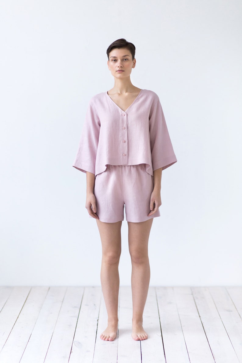 May include: A woman wearing a light pink linen pajama set with a button-up top and shorts.