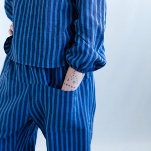 May include: A long-sleeved top and matching pants set featuring a vertical striped pattern in alternating shades of dark blue and bright blue. The top has gathered cuffs at the wrists, and the pants include a visible pocket on the front side.