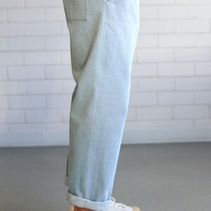May include: Light blue denim pants with a relaxed fit, cuffed at the ankles. The pants have a single pocket on the side. Paired with white canvas sneakers with a brown rubber sole.