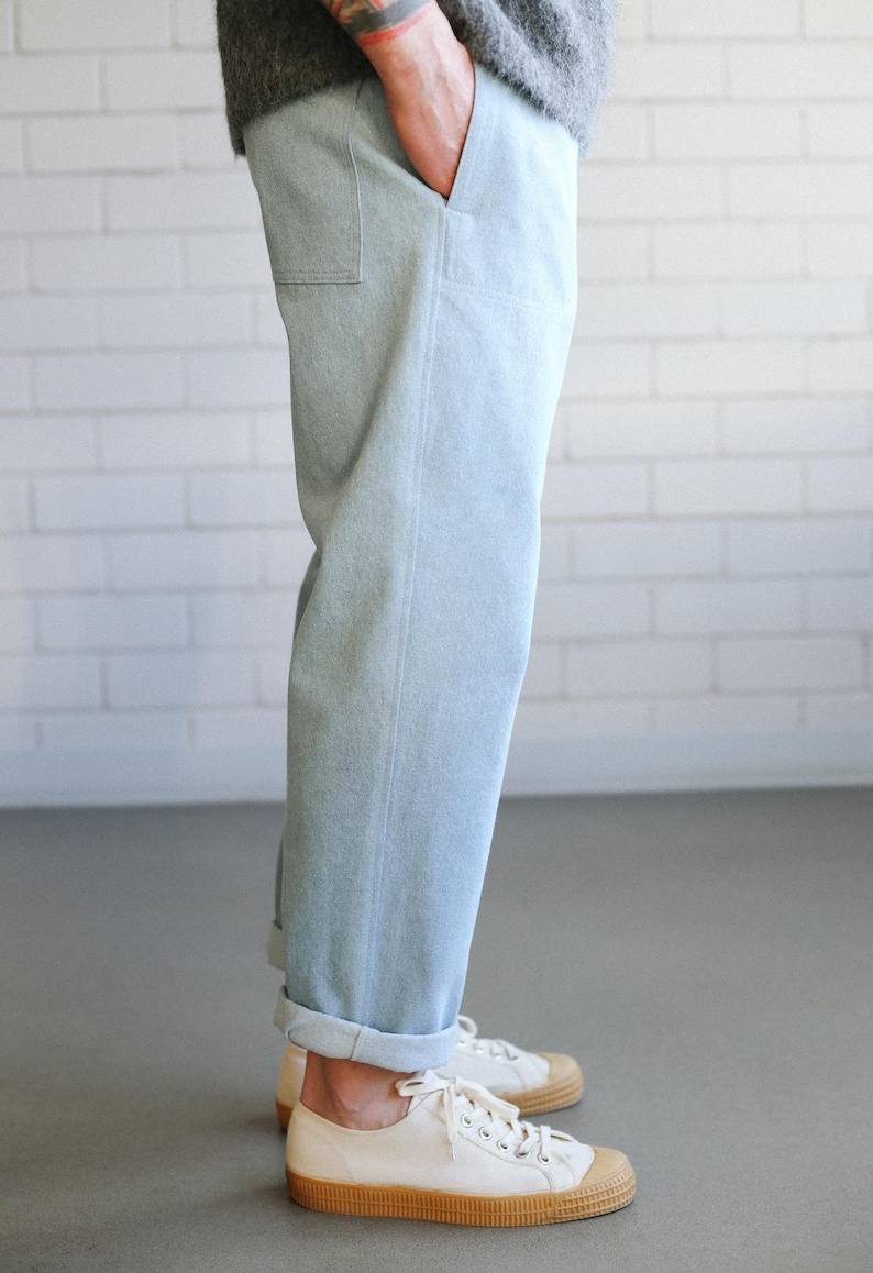 May include: Light blue denim pants with a relaxed fit, cuffed at the ankles. The pants have a single pocket on the side. Paired with white canvas sneakers with a brown rubber sole.