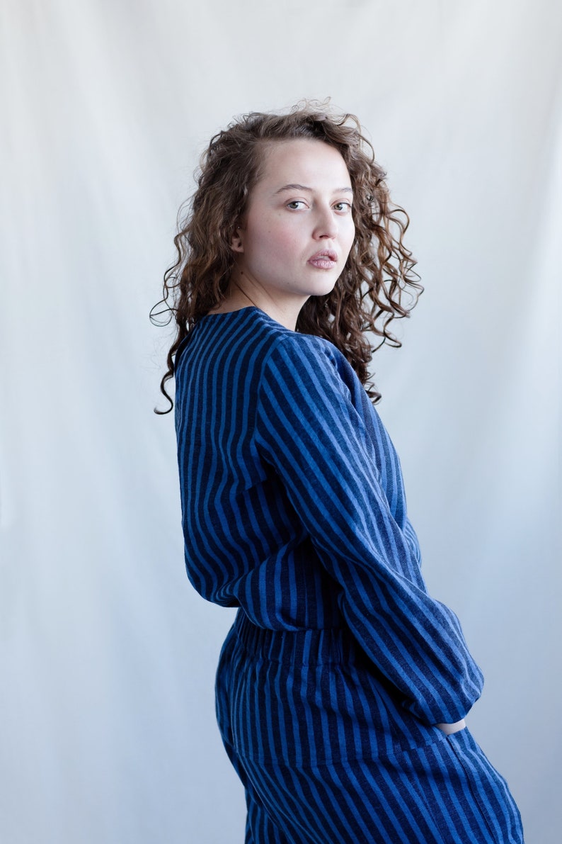 May include: A long-sleeved top and matching pants set featuring a vertical striped pattern in alternating shades of dark blue and medium blue. The garment has a round neckline, a relaxed fit, and an elasticized waistband on the trousers.