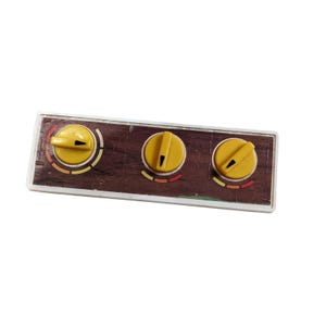 May include: A rectangular control panel with three yellow knobs. The panel has a wood-grain appearance with a white border. Each knob has a black indicator line and is surrounded by colored markings.