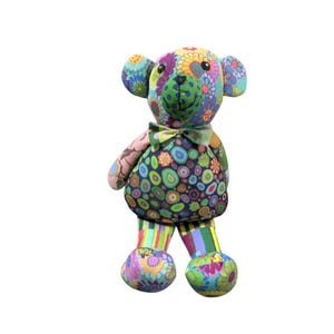 May include: A brightly coloured stuffed bear with a floral design. The bear has a green bow tie and striped legs. The bear's body is covered in a variety of floral patterns in shades of blue, green, purple, and pink.