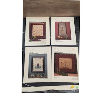 May include: Four Sheepish Designs cross-stitch patterns. Each pattern features a framed design with detailed stitching, including floral and geometric elements. The color palette includes reds, blues, and greens. The patterns are titled "In the Thick of the Fray", "More Above", "The Garden Path", and "Simple Guidance".