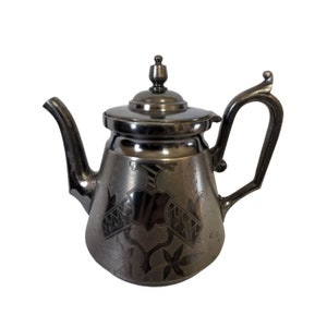 May include: A silver teapot with an ornate design. The teapot has a round body and a curved spout. The handle is attached to the side of the teapot.