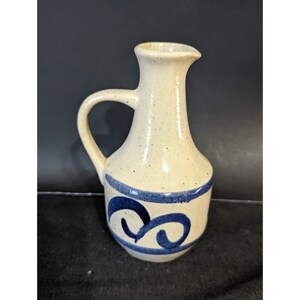 May include: A small, white ceramic pitcher with a blue and white swirl design. The pitcher has a handle and a spout.