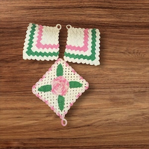 May include: Three handmade crochet pot holders. Two are square with white, green, and pink scalloped edges. The third is diamond-shaped with a pink rose and green leaves in the center. All have a loop for hanging.
