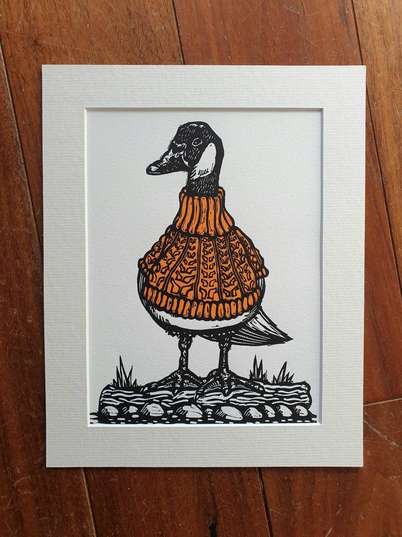 K&ouml;nnte beinhalten: Eine Schwarzwei&szlig;illustration einer Gans, die einen orangefarbenen Strickpullover tr&auml;gt. Die Gans steht auf einem felsigen Untergrund.