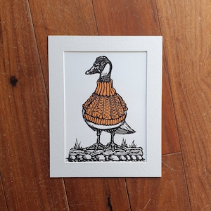 K&ouml;nnte beinhalten: Eine Schwarzwei&szlig;illustration einer Gans, die einen orangefarbenen Strickpullover tr&auml;gt. Die Gans steht auf einem kleinen Stein mit Gras drumherum.