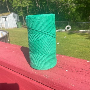 May include: A roll of green twine, likely used for gardening or crafts, is sitting on a red wooden surface.