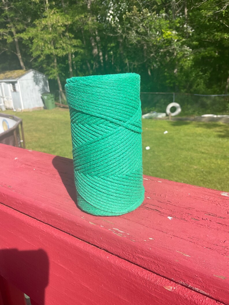 May include: A roll of green twine, likely used for gardening or crafts, is sitting on a red wooden surface.
