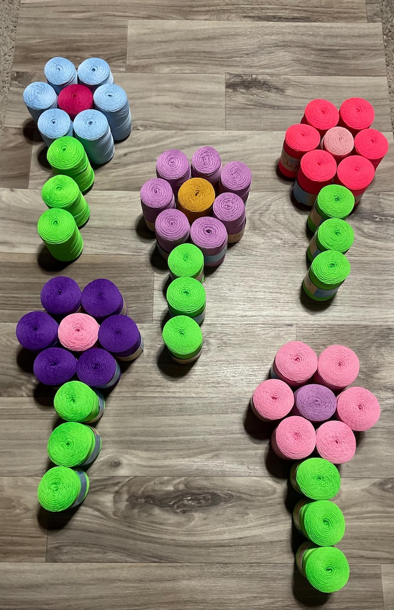 May include: Arrangement of colorful spools of thread, crafted to resemble flowers. The 'petals' are various shades of pink, purple, blue, and yellow, with green stems. The spools are arranged on a wooden surface.