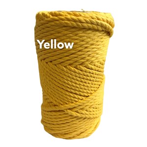 May include: A spool of bright yellow macrame cord featuring a thick, twisted rope construction. The word Yellow is printed in white text on the upper left side of the cord spool. The cord is wound tightly into a cylindrical shape.