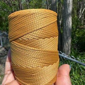 May include: A spool of golden-yellow nylon cord. The cord is tightly wound, showing a gradient of color from light to dark. The texture of the cord is visible, suggesting a durable material suitable for various crafting projects.