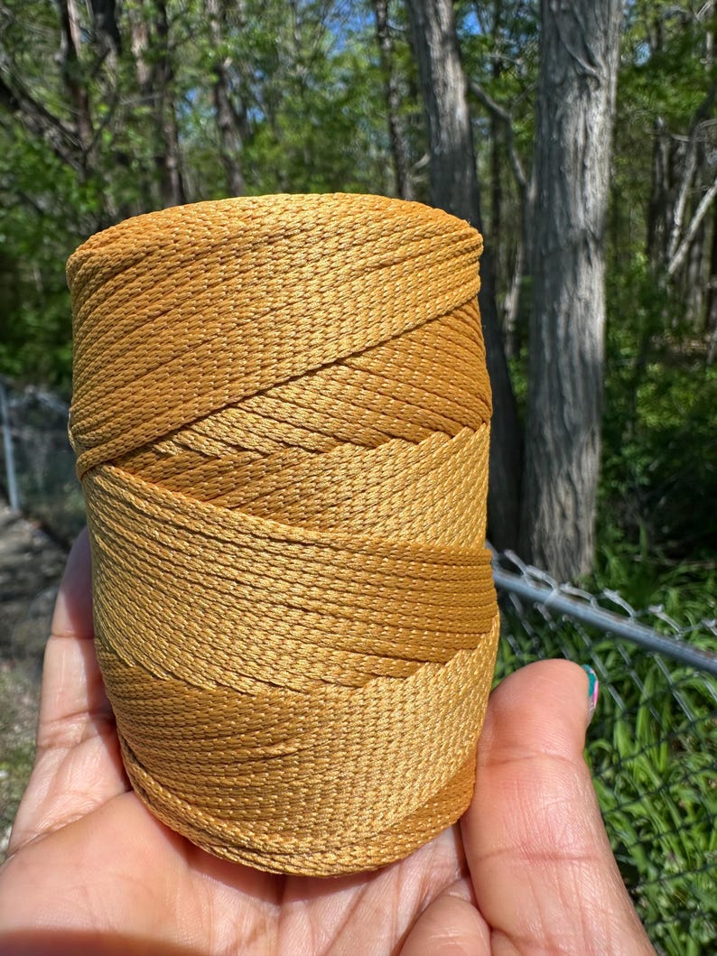 May include: A spool of golden-yellow nylon cord. The cord is tightly wound, showing a gradient of color from light to dark. The texture of the cord is visible, suggesting a durable material suitable for various crafting projects.