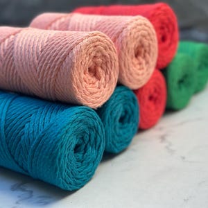May include: A stack of colorful yarn spools in pink, teal, red, and green. The yarn is arranged in a rainbow pattern.