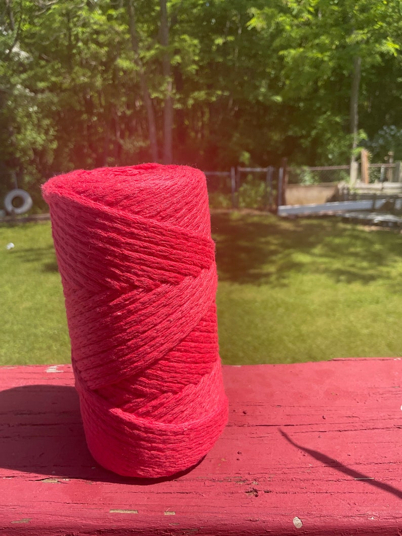May include: A roll of bright red yarn, likely cotton, is sitting on a red wooden surface. The yarn is wound tightly and has a rough texture.