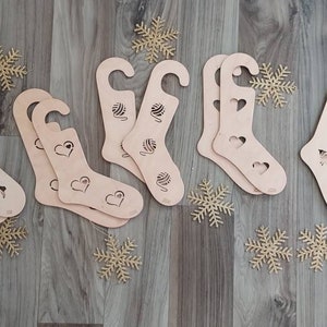 Könnte beinhalten: Acht hölzerne Sockenhalter mit verschiedenen Designs. Die Designs beinhalten Herzen, Wollknäuel und Lamas. Die Halter sind alle hellbraun und haben einen Haken oben.