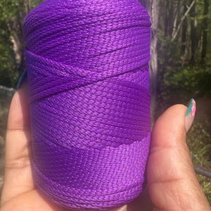 May include: A spool of vibrant purple thread. The thread is tightly wound, creating a cylindrical shape. The color is a rich, saturated purple, with a slight sheen. The thread appears to be made of a smooth, durable material, suitable for various crafting projects.