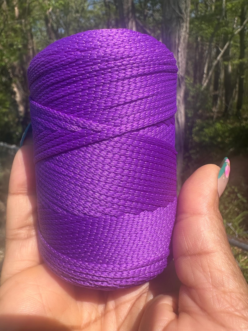 May include: A spool of vibrant purple thread. The thread is tightly wound, creating a cylindrical shape. The color is a rich, saturated purple, with a slight sheen. The thread appears to be made of a smooth, durable material, suitable for various crafting projects.
