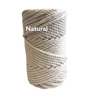 May include: A cylindrical spool of thick, off-white twisted cotton rope. The rope is wound in a tight, continuous coil, creating a textured surface. The word Natural is printed in white letters on the upper left side of the rope spool.