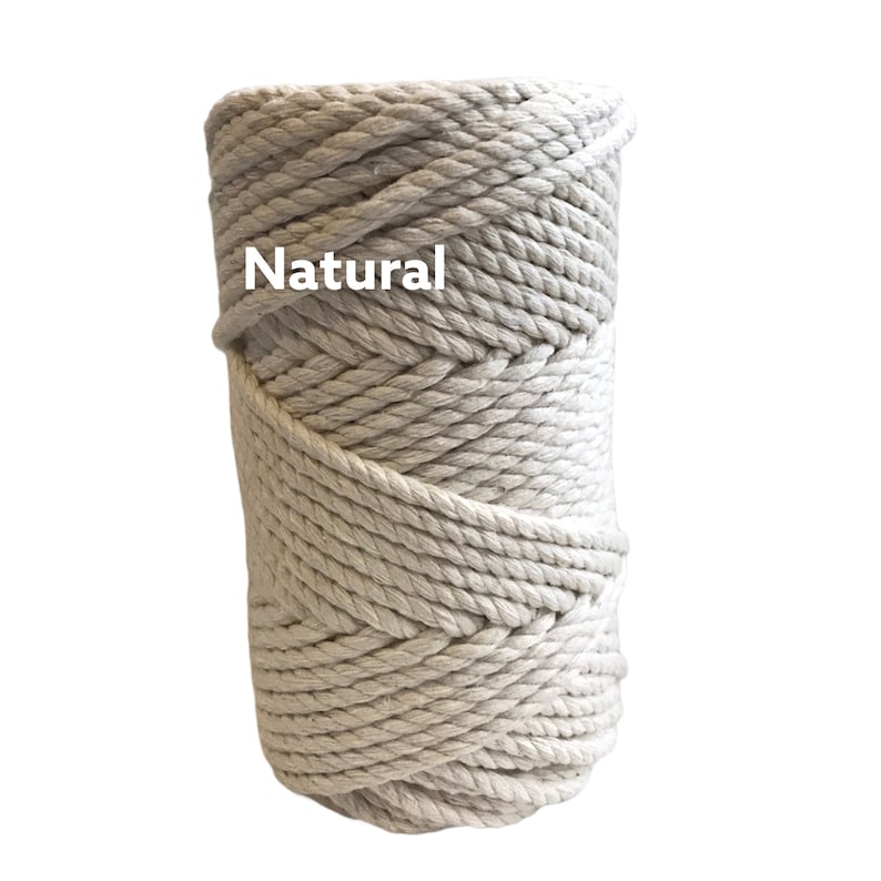 May include: A cylindrical spool of thick, off-white twisted cotton rope. The rope is wound in a tight, continuous coil, creating a textured surface. The word Natural is printed in white letters on the upper left side of the rope spool.