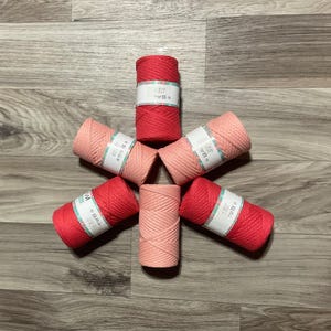 May include: Six spools of cotton rope in two colors: pink and red. The spools are arranged in a star shape on a wood floor. Each spool has a label with Chinese characters.