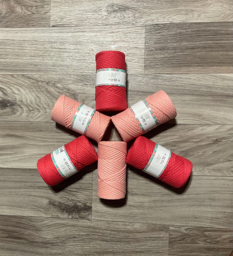 May include: Six spools of cotton rope in two colors: pink and red. The spools are arranged in a star shape on a wood floor. Each spool has a label with Chinese characters.