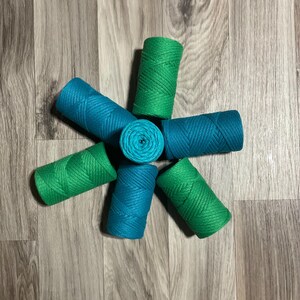 May include: Six spools of twine in teal and green colors arranged in a star shape on a wood floor.